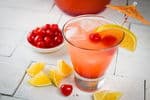 Shirley Temple Punch on white wooden background, maraschino cherries and lemons on the side.
