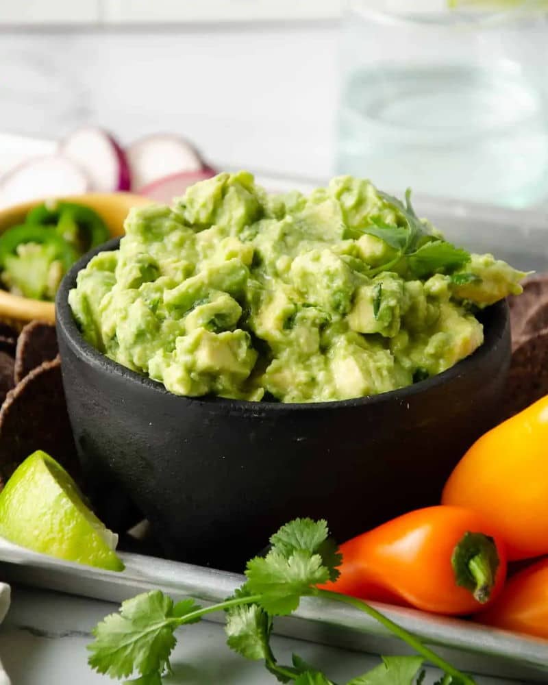 Guacamole in black bowl on tray with veggies.