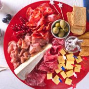 Top view of charcuterie board with red, white and blue star toothpicks on red plate.