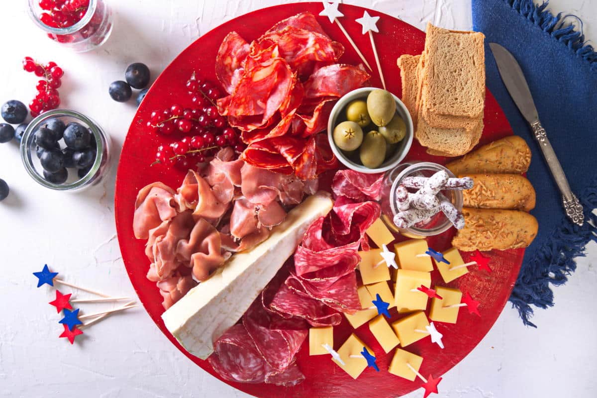 Top view of charcuterie board with red, white and blue star toothpicks on red plate.