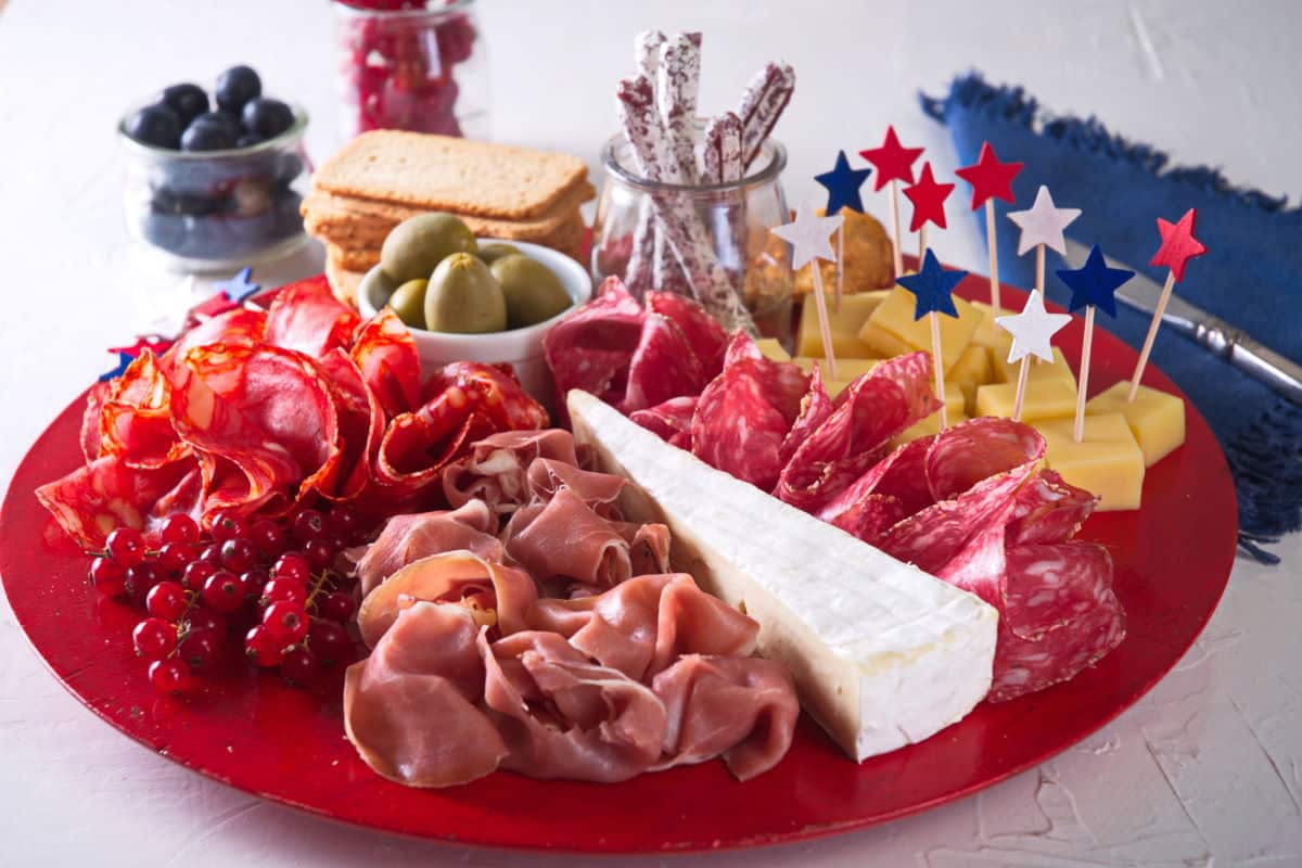 Charcuterie board with red, white and blue star toothpicks on red plate.