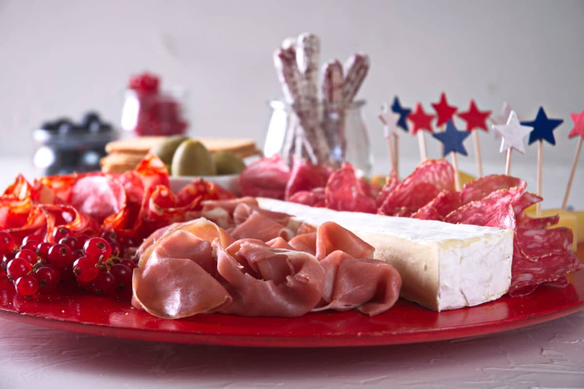 Front view of charcuterie board with red, white and blue star toothpicks on red plate.