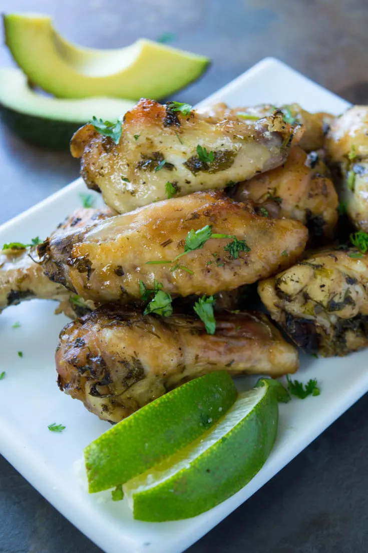 Chicken wings on white plate, limes and avocado slices on the side.