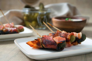 Grilled, bacon wrapped pickles on toothpicks, on a white plate.
