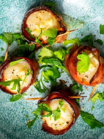 Bacon wrapped scallops with butter sauce in blue dish.