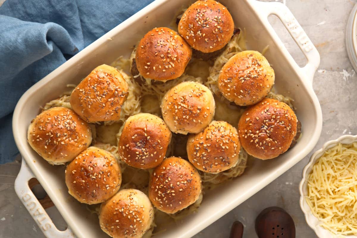 Bison sliders in casserole dish with shredded cheese on the side.