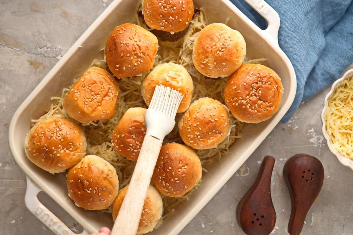 Bison sliders prepped in casserole dish with pastry brush.