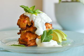 Crab cakes stacked on a clear glass plate with avocado and yogurt sauce.