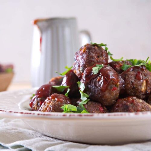 Front view of bison meatballs with BBQ sauce and parsley on white plate.