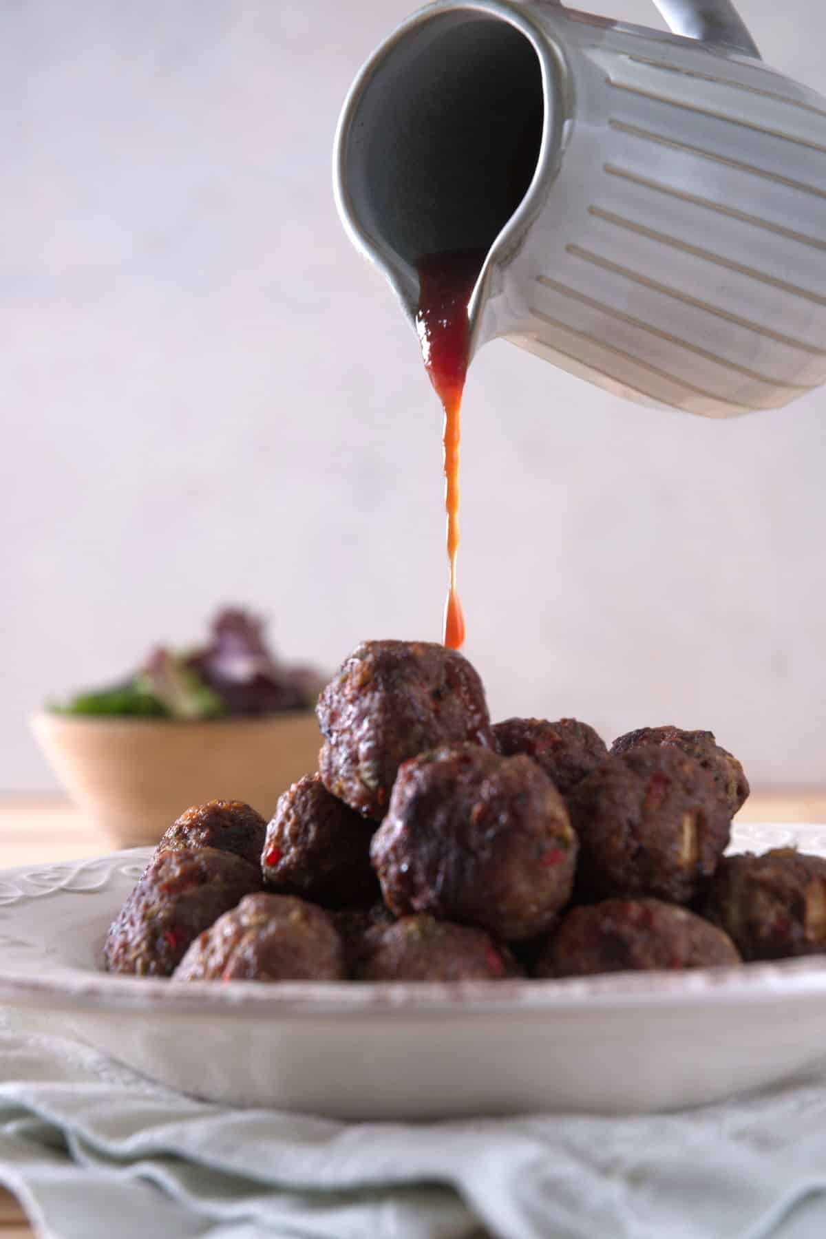 Bison meatballs on white plate with BBQ sauce pouring over.