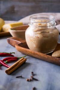 Banana ketchup in a small jar, chili peppers and a cinnamon stick on the side.