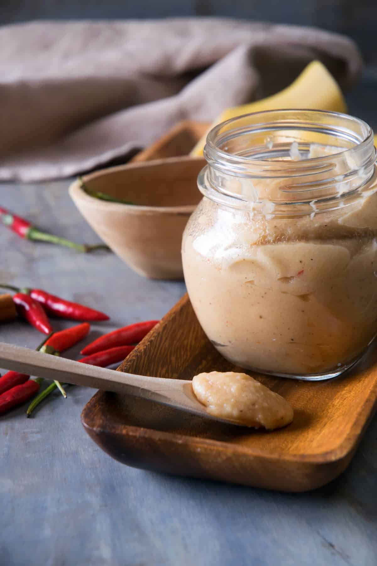 Banana ketchup in a small jar and on a small spoon, chili peppers on the side.