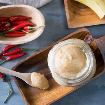 Banana ketchup in a small jar and on a small spoon on wooden dish. Thai red chili peppers in a small wooden bowl on the side.