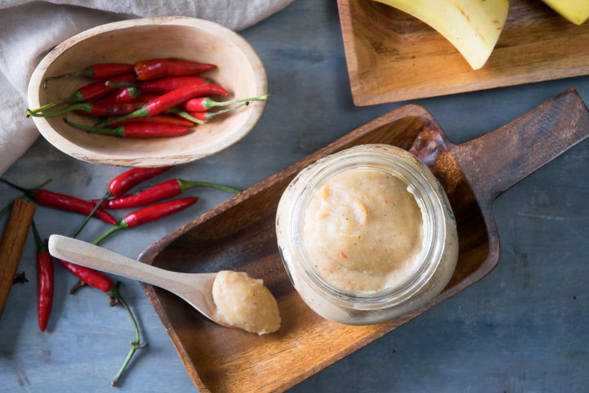 Banana ketchup in a small jar and on a small spoon on wooden dish. Thai red chili peppers in a small wooden bowl on the side.