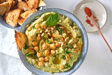 Basil hummus with pine nuts in blue bowl, toast points on the side..