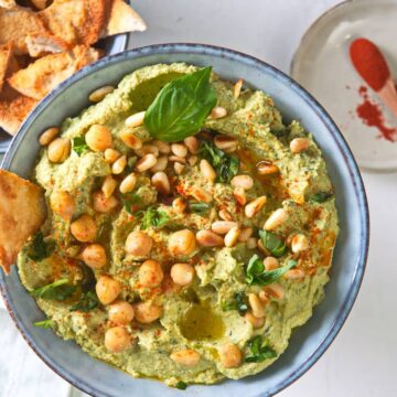 Basil hummus with pine nuts in blue bowl, toast points on the side..