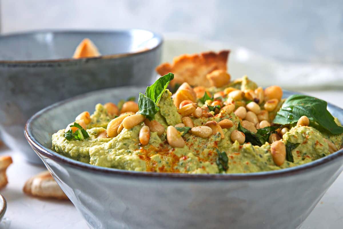 Basil hummus with pine nuts in blue bowl.