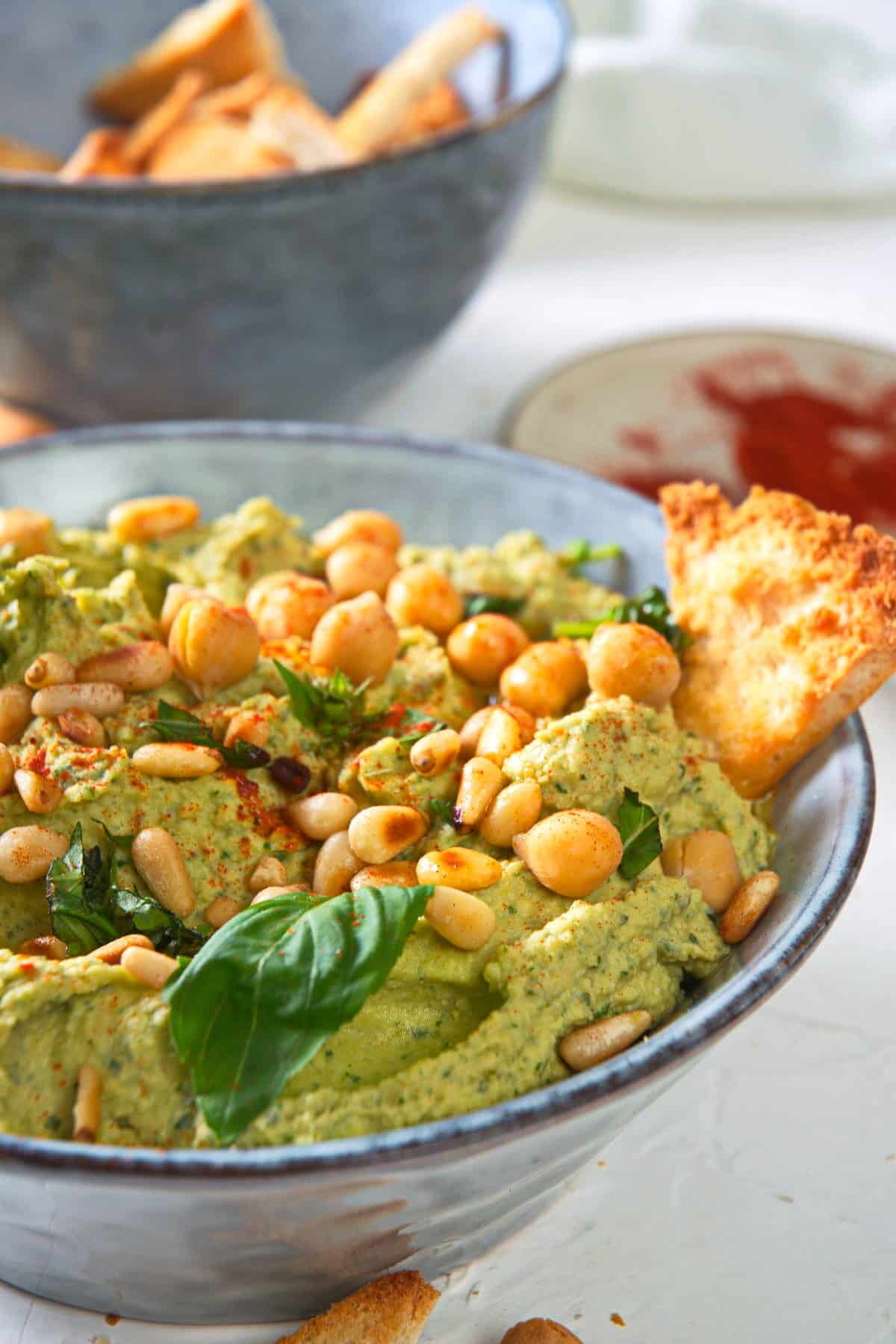 Basil hummus with pine nuts and a toast point in blue bowl.