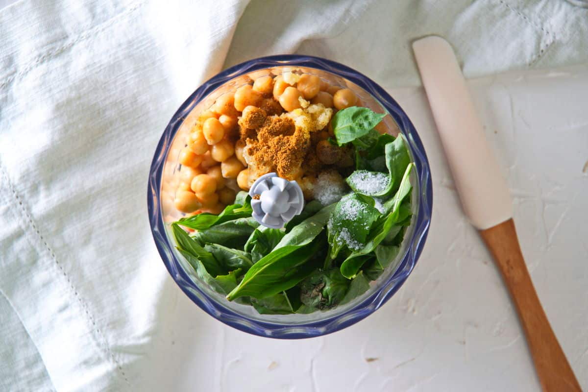 Basil and chickpeas in food processor, spatula on the side.