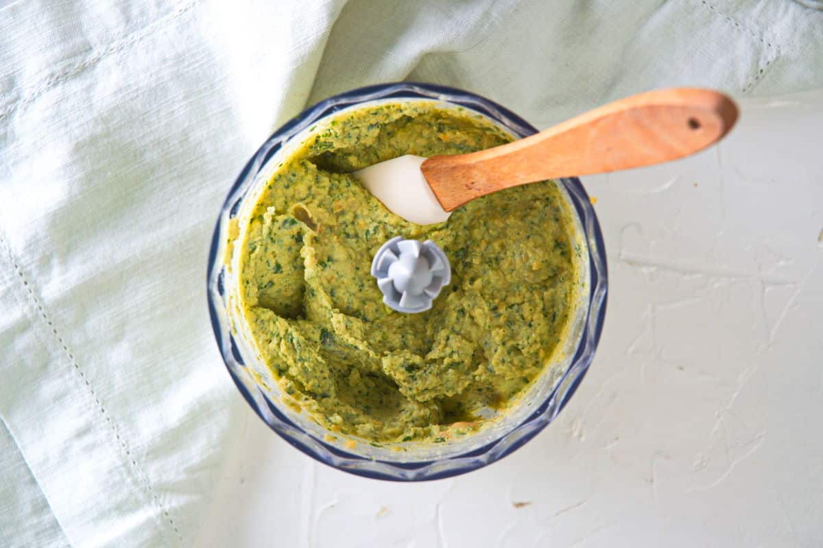 Basil hummus in food processor with spatula.