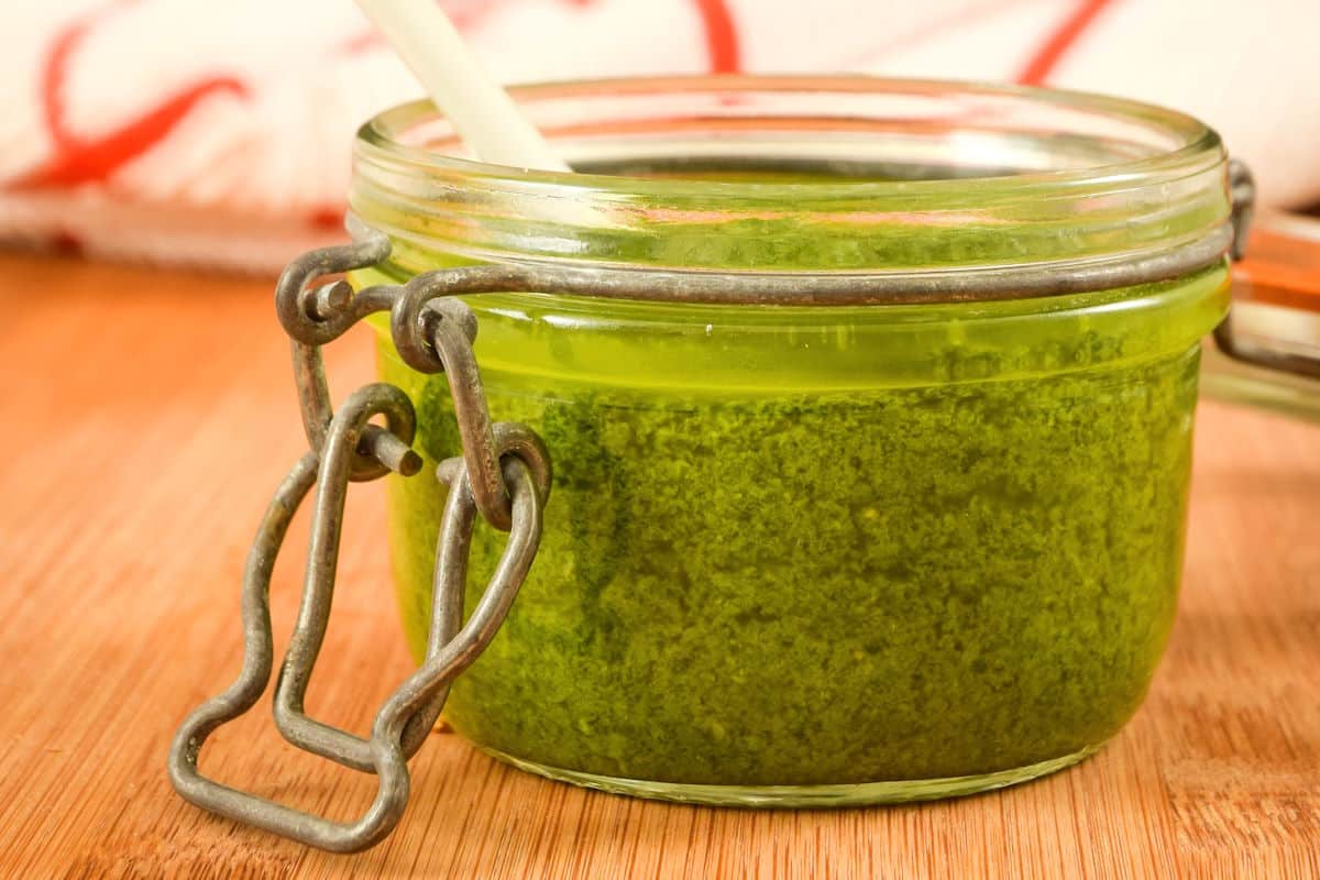 Basil pesto in a small jar on wooden table.