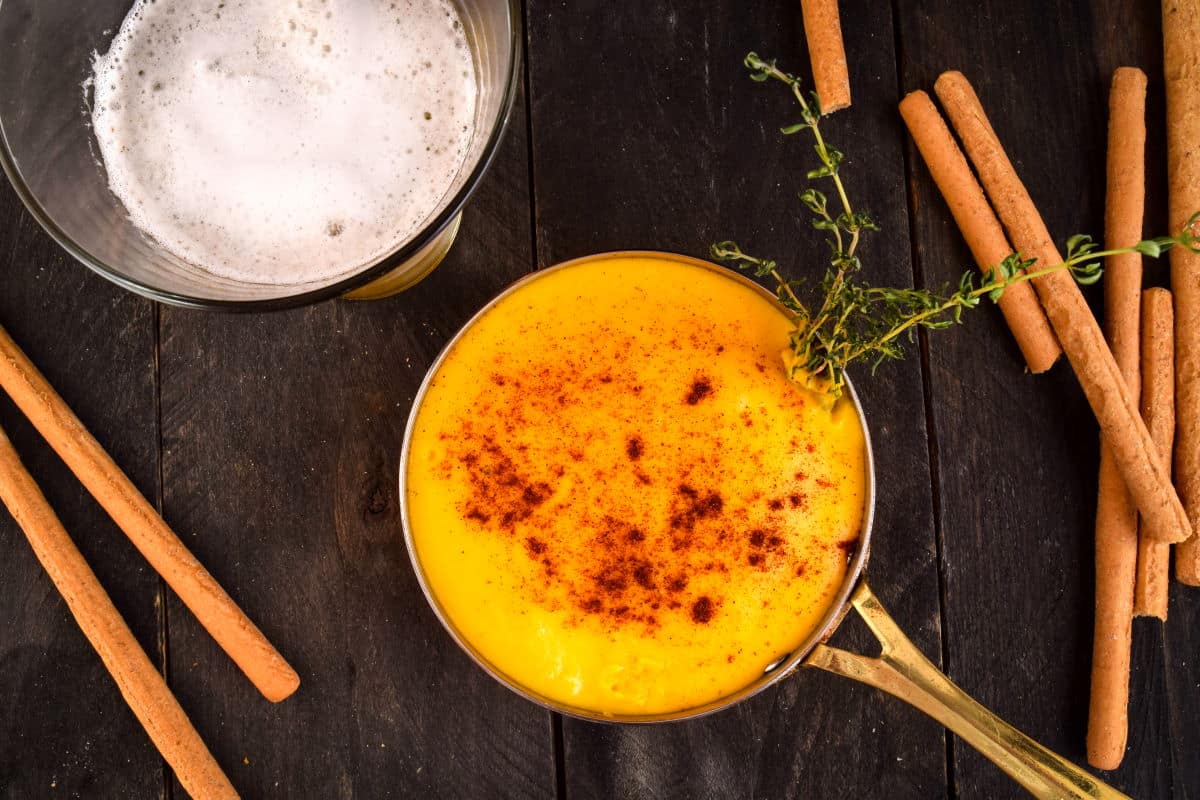 Beer cheese dip in a copper pot with bread sticks and a glass of beer on the side.