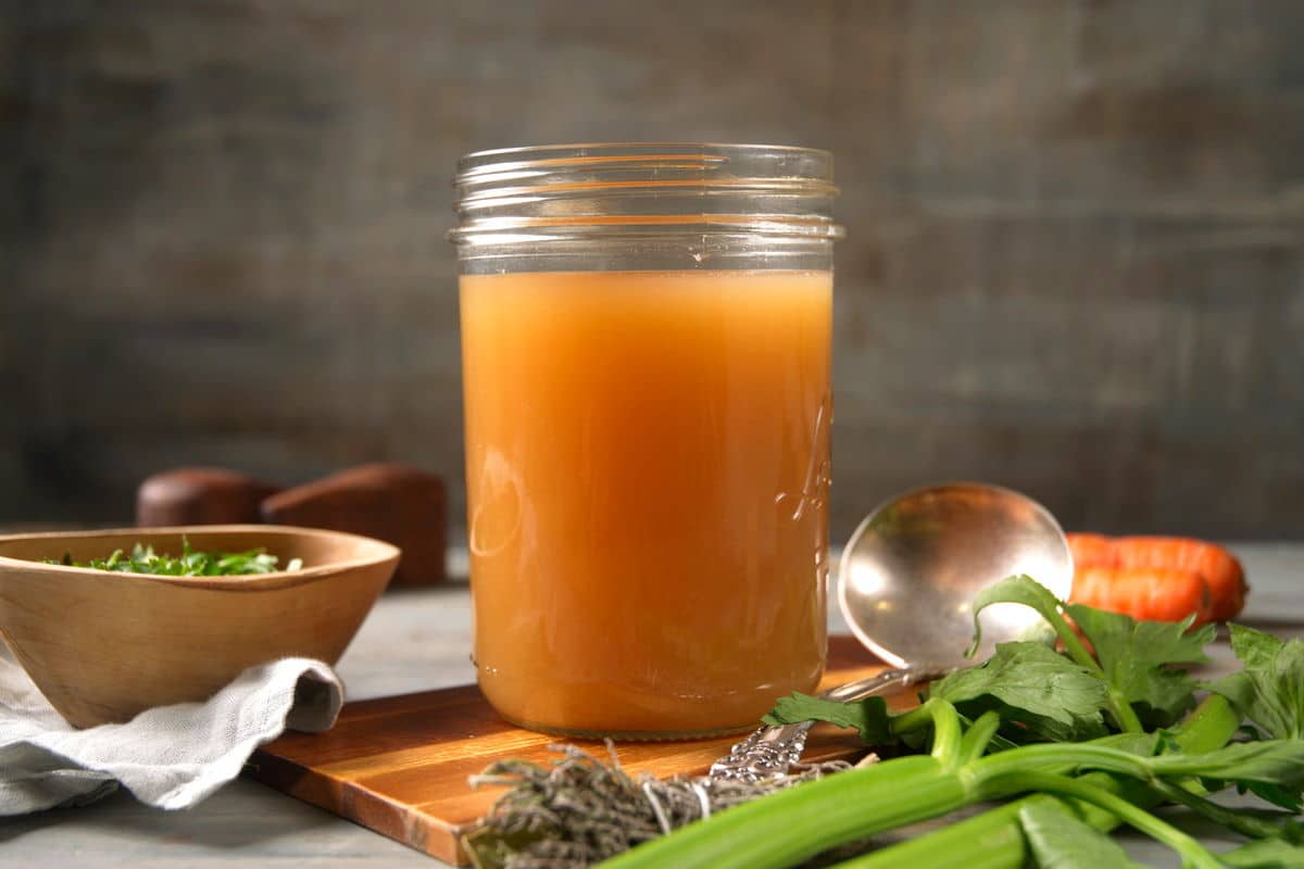 Bison bone broth in a small jar with dark background. Vegetables on the side.