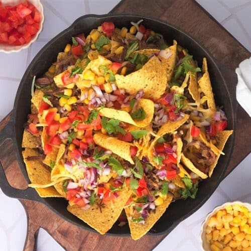 Top view of bison brisket nachos in cast iron pan on cutting board.