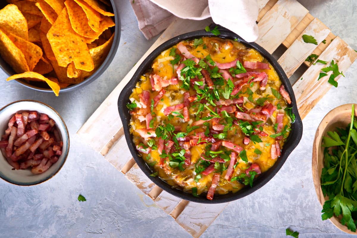 Bison dip in cast iron skillet with tortilla chips and bacon bits on the side.