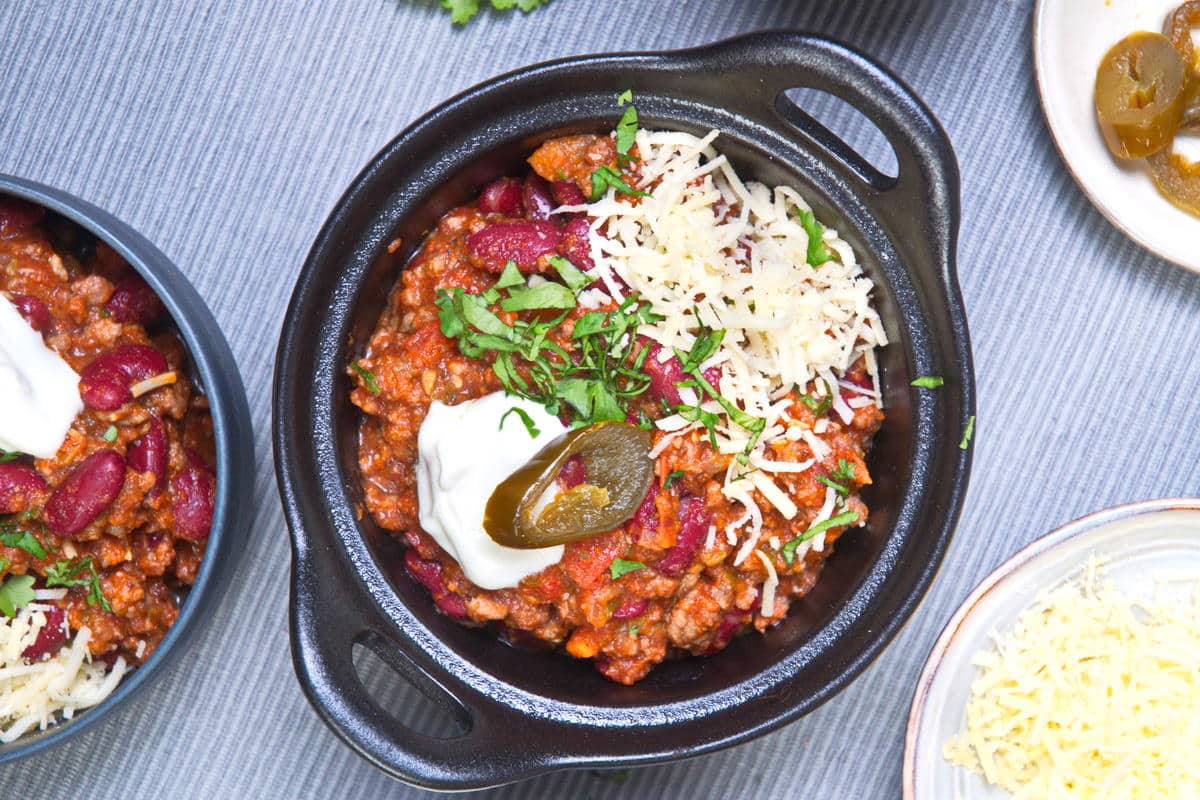 Top view of ground bison chili with cheese, jalapenos, sour cream and cilantro in black bowl.