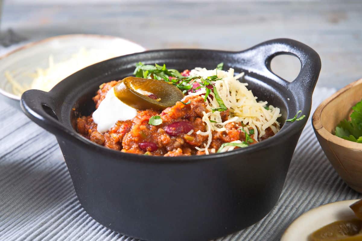 Bison chili with cheese, jalapenos and cilantro in black bowl.