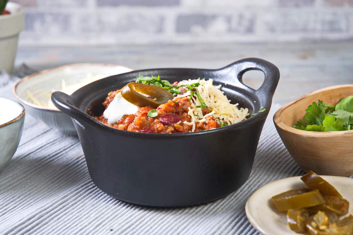 Bison chili with cheese, jalapenos and cilantro in black bowl.