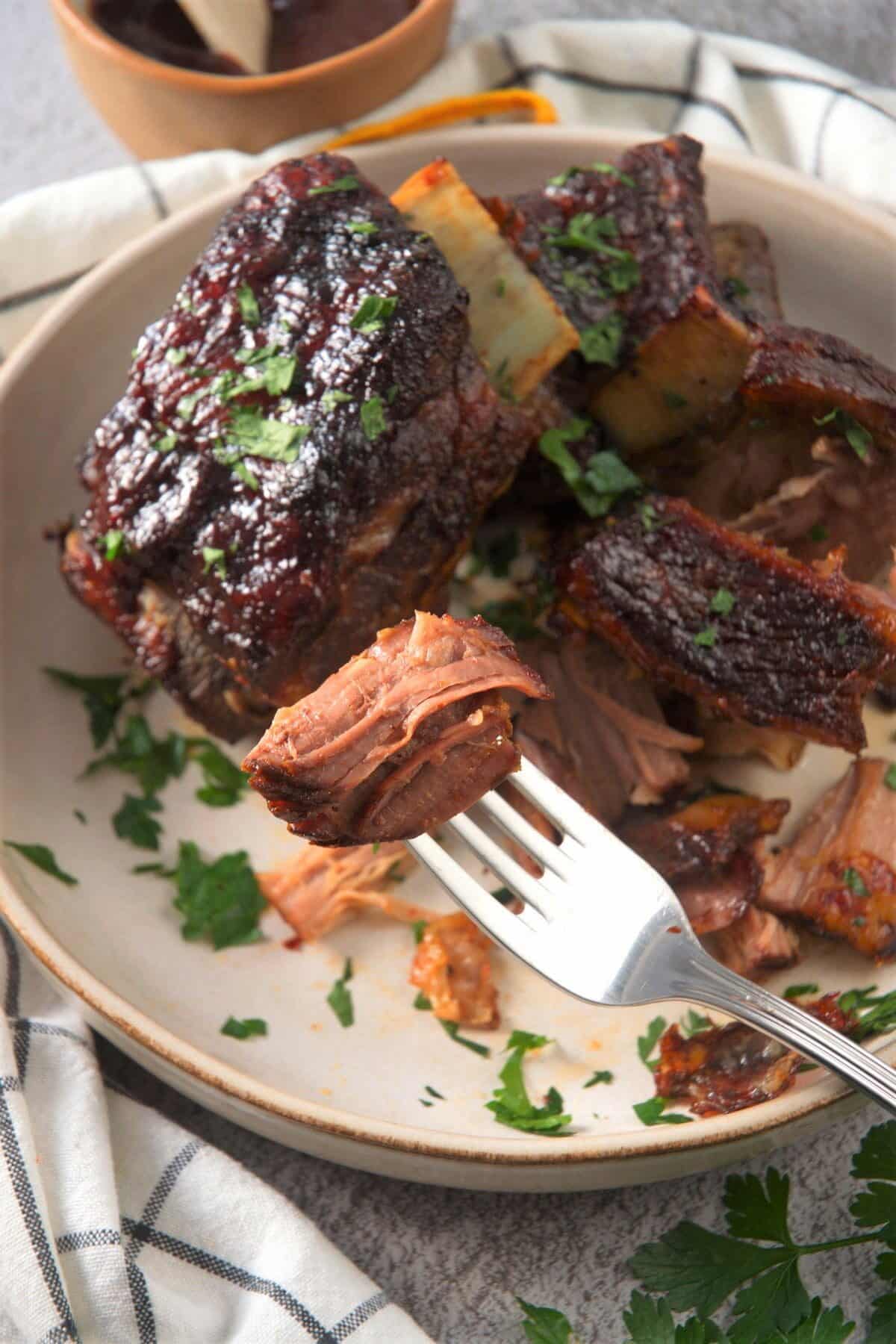 Cooked BBQ bison ribs in white dish and on a fork.