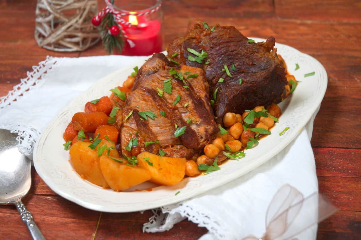 Sliced bison roast on a white serving dish with vegetables. Christmas candle in the background.