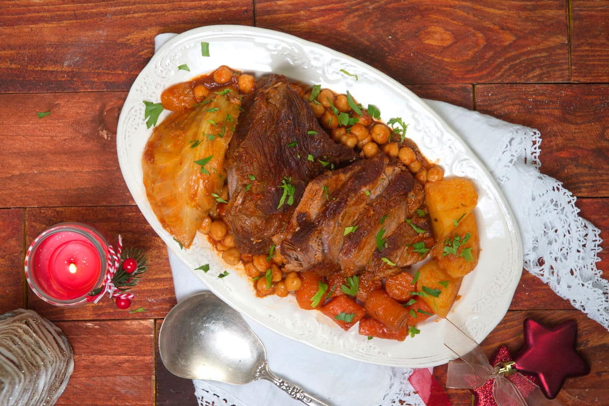 Sliced bison roast on a white serving dish with vegetables. Christmas candle and decorations on the side.