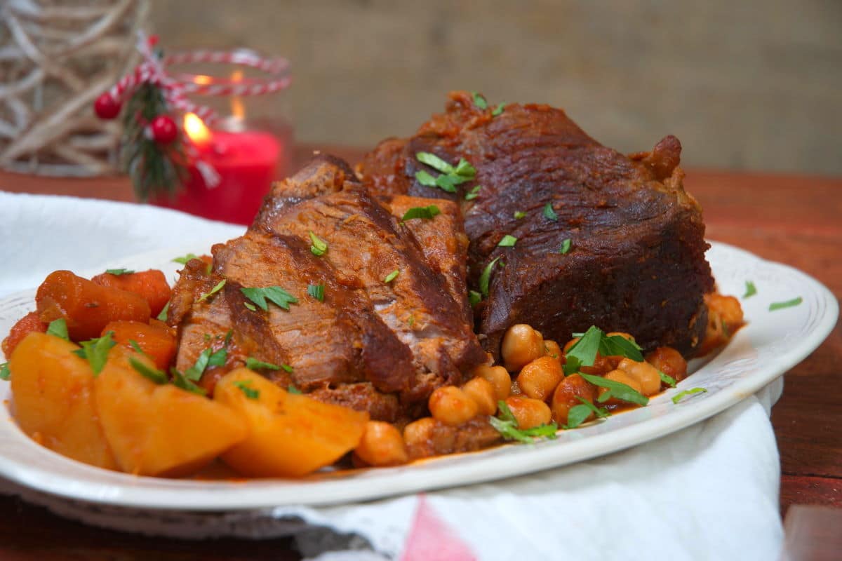 Sliced bison roast on a white serving dish with vegetables. Christmas candle in the background.