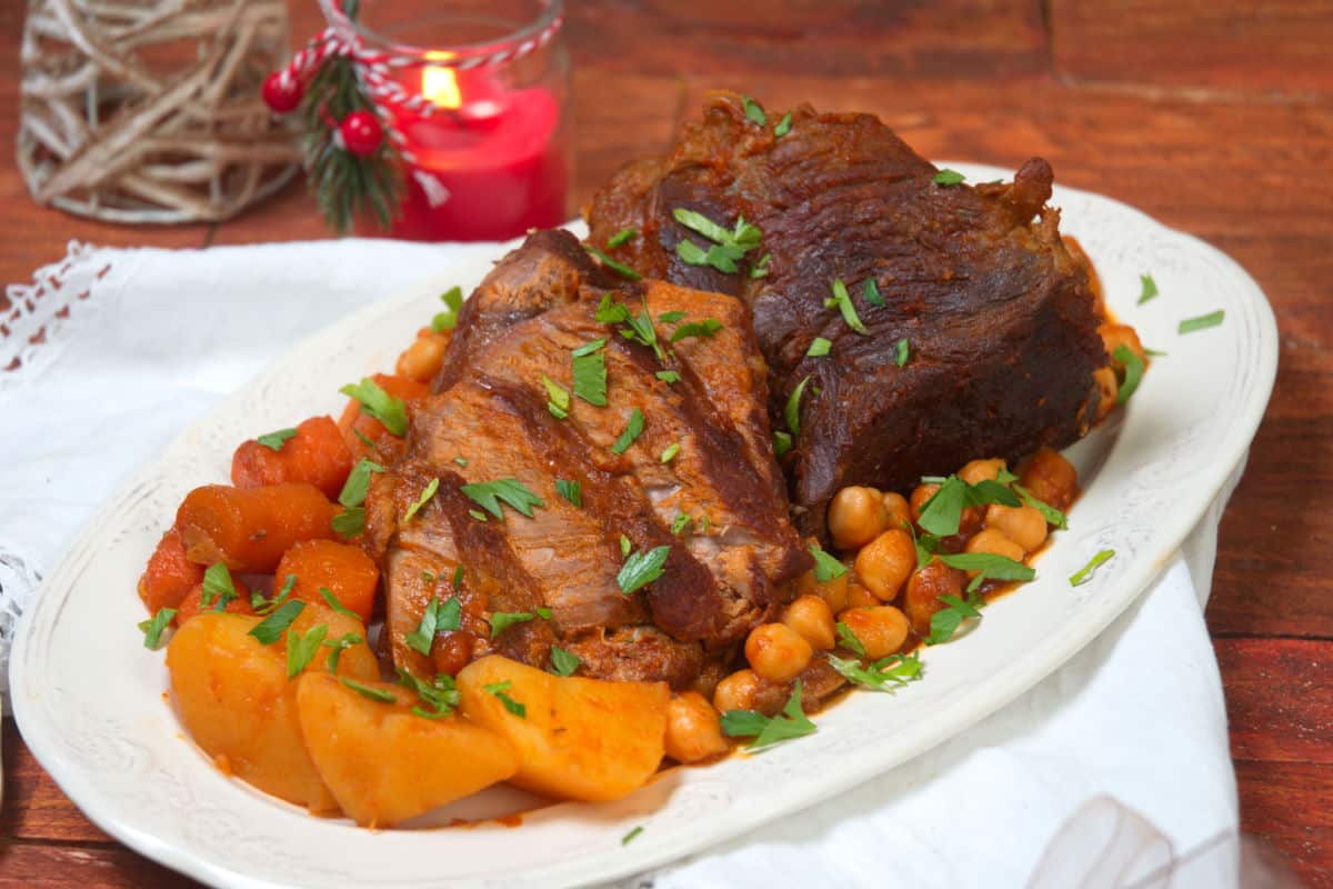 Sliced bison roast on a white serving dish with vegetables.