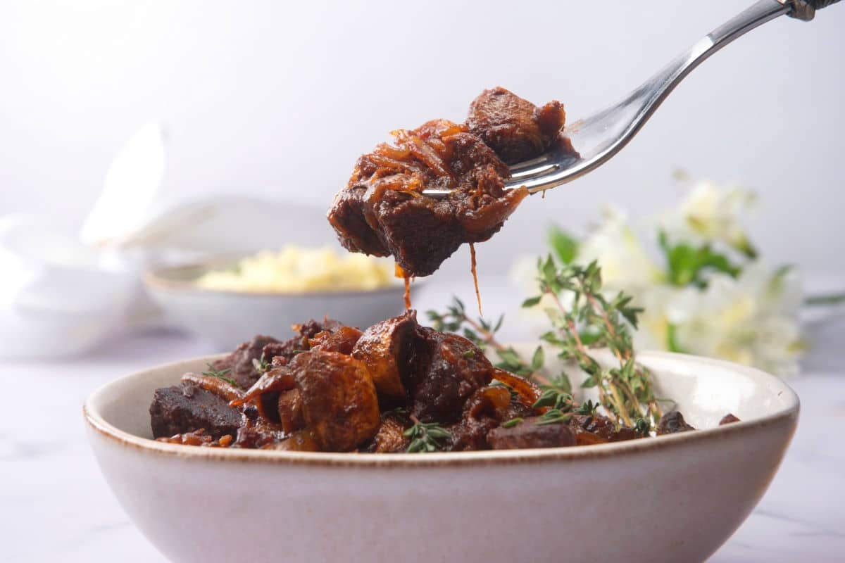 Bison stew and fresh thyme in a light-colored bowl with a fork.