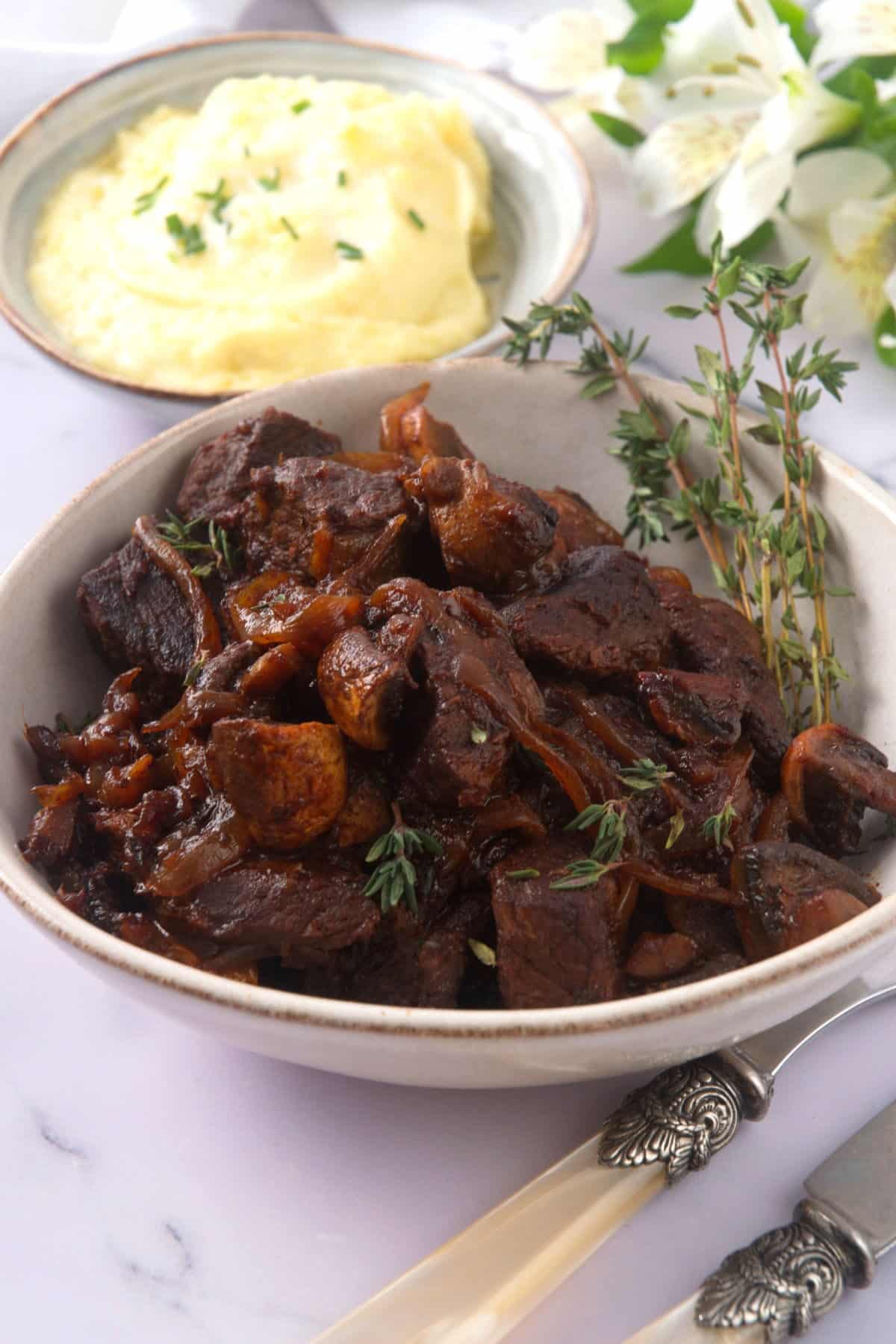 Bison stew with fresh thyme in a light-colored bowl, mashed potatoes on the side.