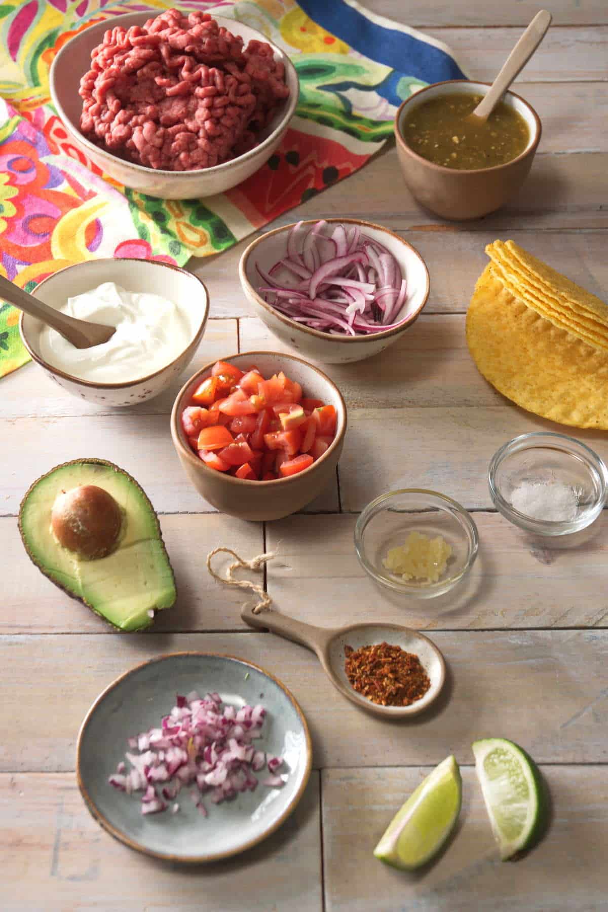 Bison taco ingredients prepped in small bowls on light wooden background.