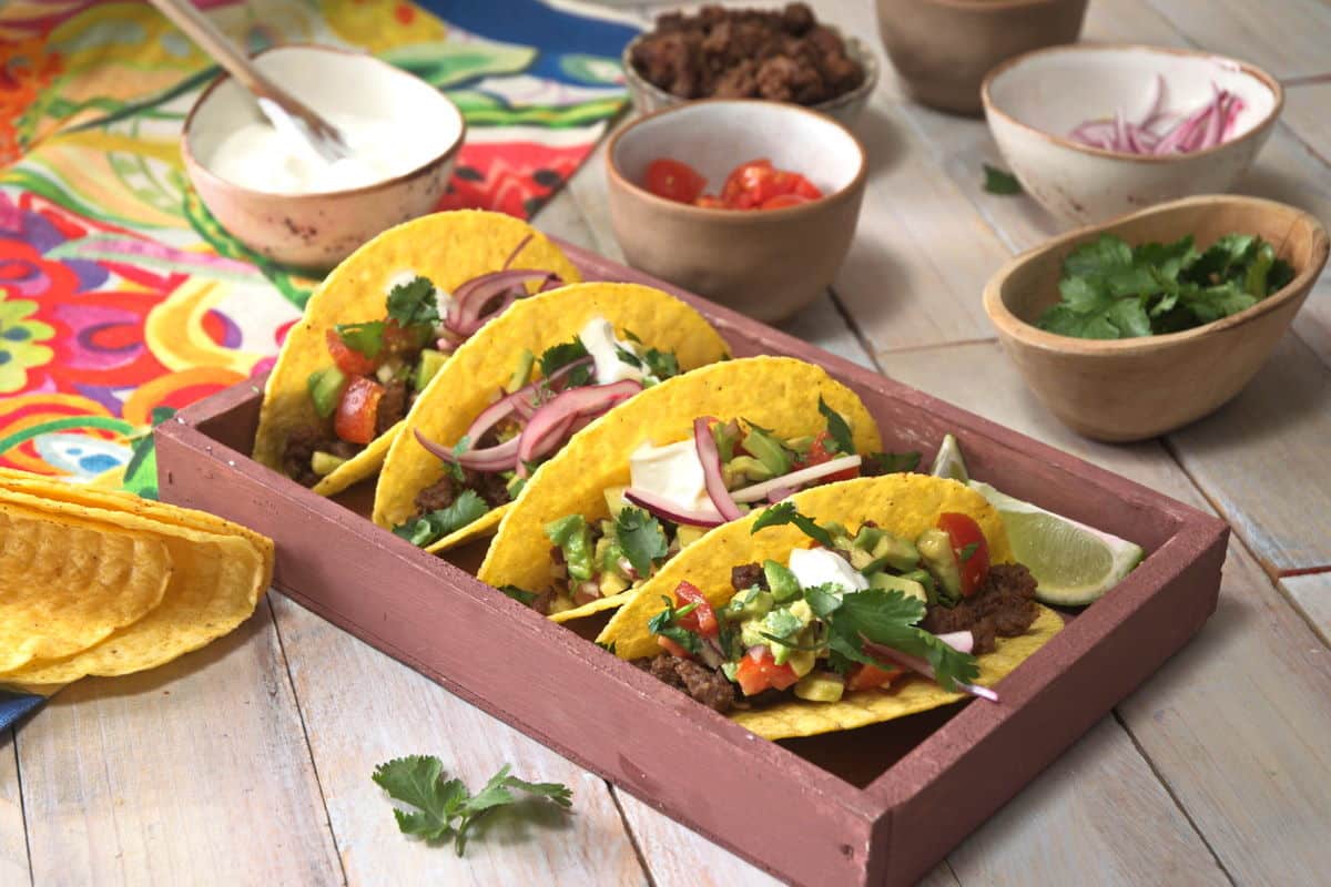 Bison tacos layered in a dish. Tomatoes, cilantro, red onion, ground bison and sour cream on the side in small bowls.