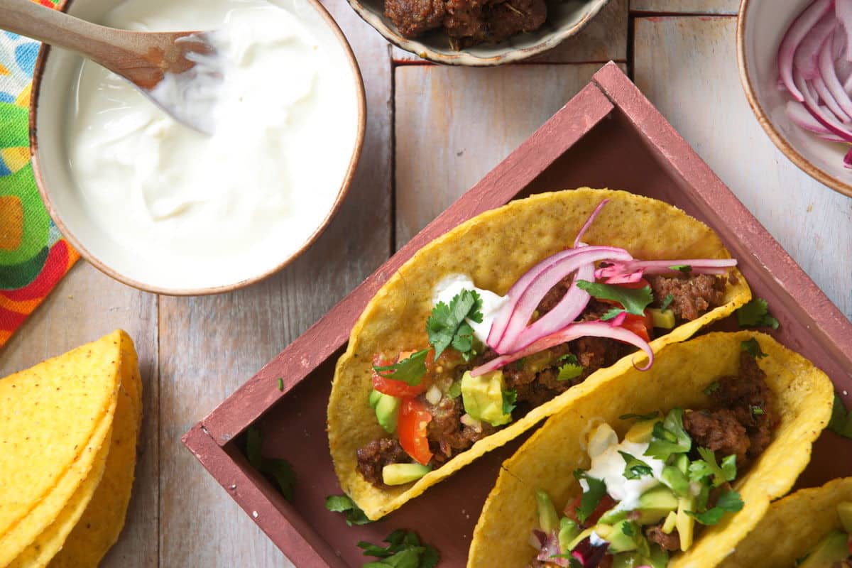 Bison hard tacos layered in a dish. Sour cream and sliced red onions on the side.