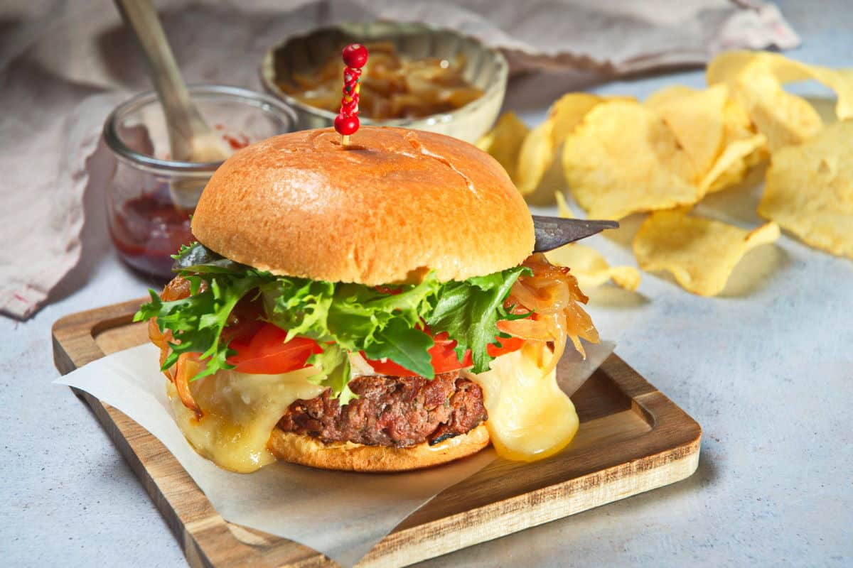 Bison burger on wooden cutting board with chips on the side.