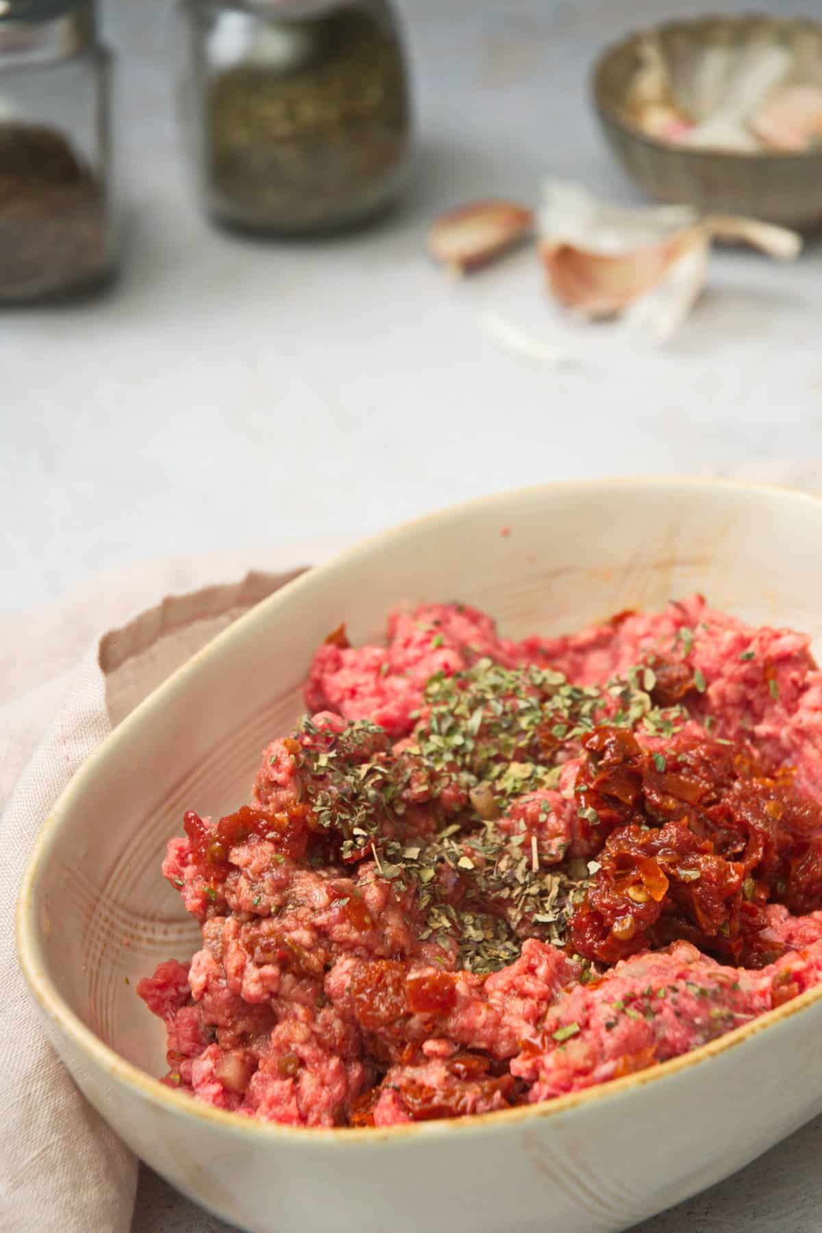 Ground raw bison meat with spices in a white dish.