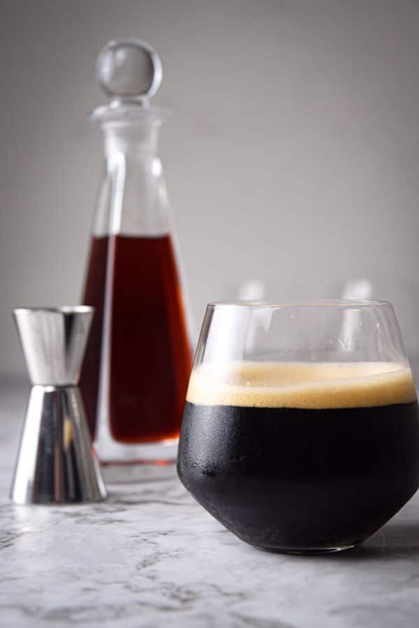 Black fog cocktail in a glass, raspberry liqueur in the background, on marble.