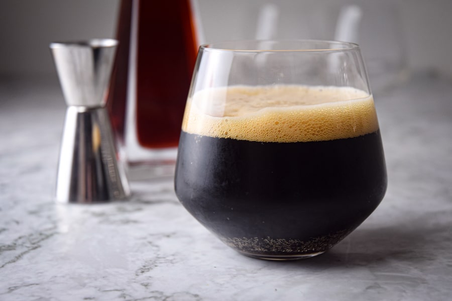 Black fog cocktail in a glass, raspberry liqueur in the background, on marble.