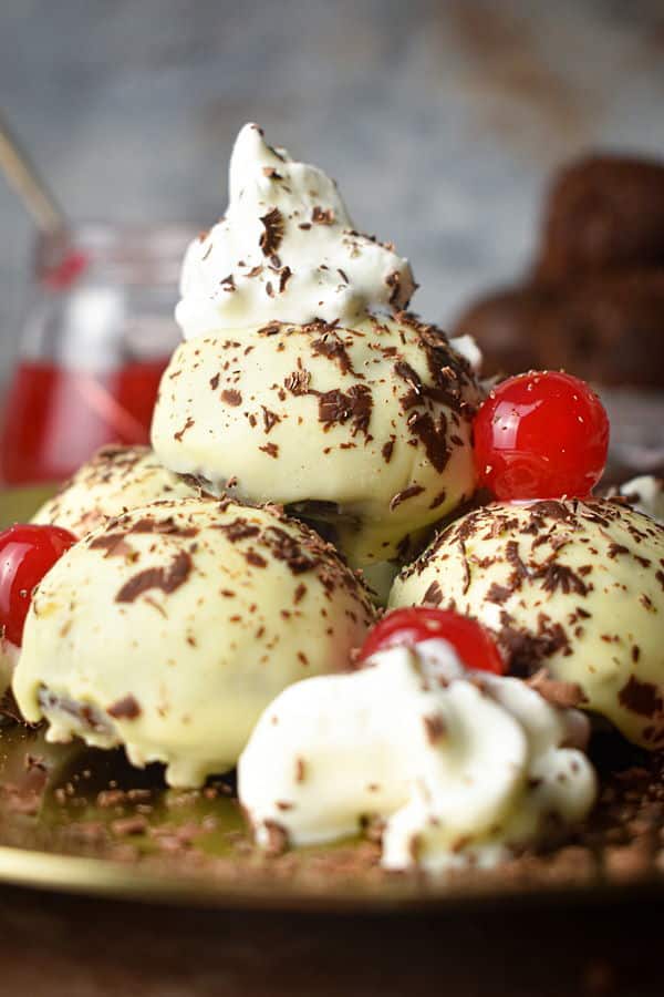 Black forest cake balls on a plate with whipped topping, cherries and chocolate shavings.