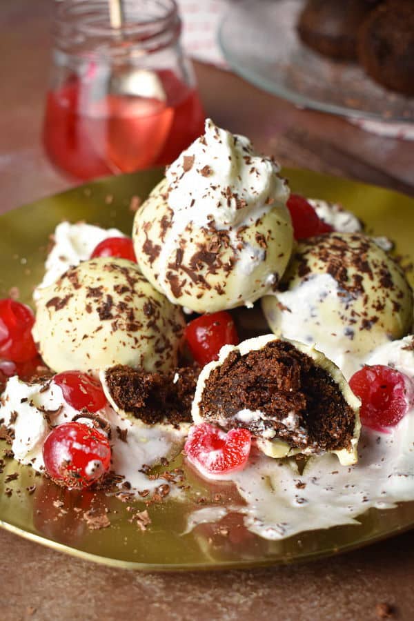 Black forest cake balls on a plate with whipped topping, cherries and chocolate shavings.