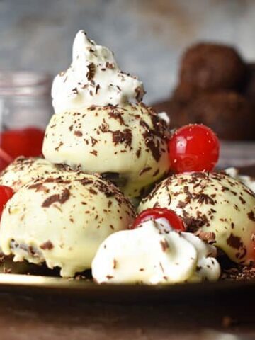 Black forest cake balls on a plate with whipped topping, cherries and chocolate shavings.