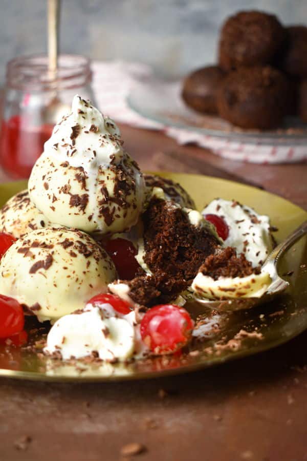 Black forest cake balls on a plate with whipped topping, cherries and chocolate shavings.